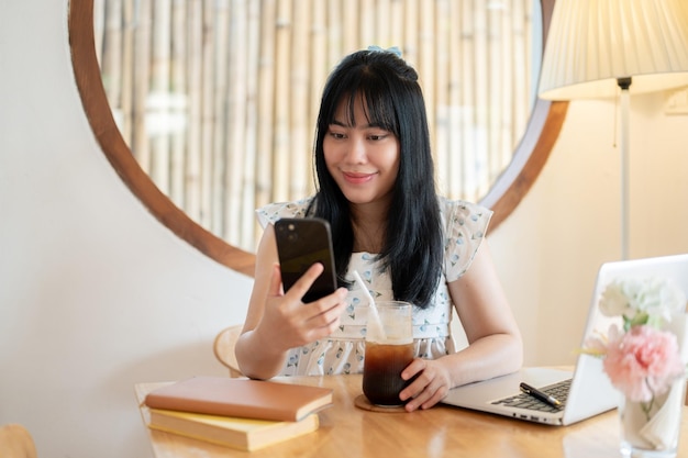 Foto een gelukkige charmante jonge aziatische vrouw ontspant zich in een koffieshop en gebruikt haar smartphone
