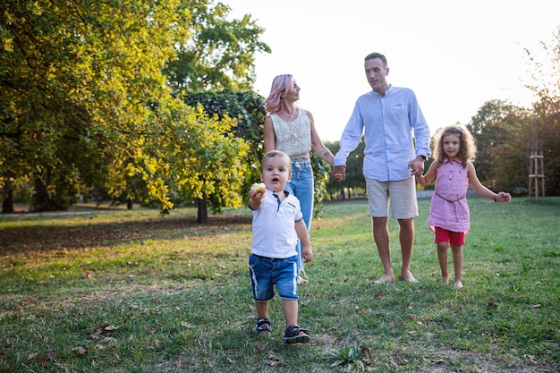 Een gelukkige familie in het park, samen zoon die een appel eet en gelukkige ouders die elkaars hand vasthouden, zus glimlachen