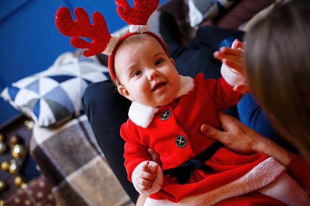 Een gelukkige familie in rode truien zit samen op de vloer. Kerst vakantie sfeer. Een kind in een kerstmankostuum. Familie relatie concept