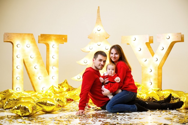 Een gelukkige familie in rode truien zit samen op de vloer. Kerst vakantie sfeer. Een kind in een kerstmankostuum. Familie relatie concept