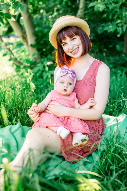 Een gelukkige familie met een picknick in de groene tuin op een zonnige lentedag: een mooie glimlachende moeder zittend op groen gras en haar dochtertje lachen op haar benen