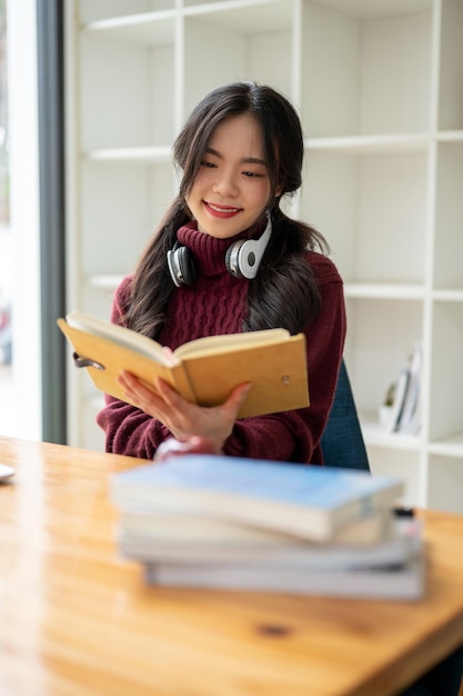 Een gelukkige jonge Aziatische studente leest een boek aan een tafel in de coffeeshop