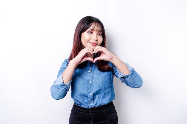 Een gelukkige jonge Aziatische vrouw die een blauw shirt draagt, voelt een romantisch hartgebaar dat tedere gevoelens uitdrukt