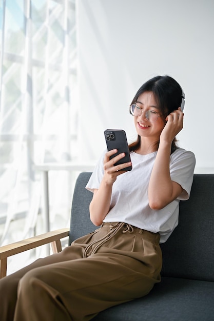 Een gelukkige jonge Aziatische vrouw geniet van de muziek op haar koptelefoon terwijl ze op een bank zit