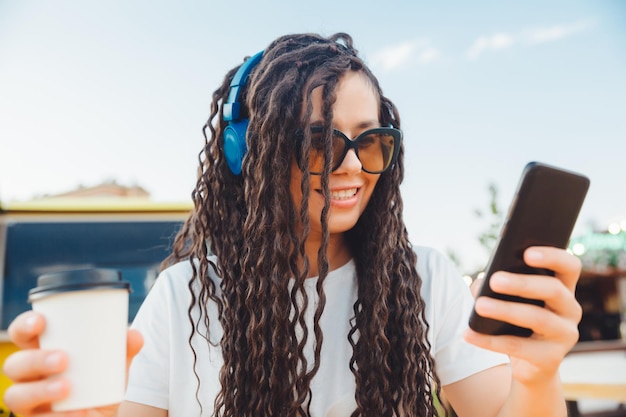 Een gelukkige jonge vrouw die een webconferentie bijwoont via een koptelefoon of een freelancer die aan een terrastafel zit, een meisje met dreadlocks communiceert via een videolink