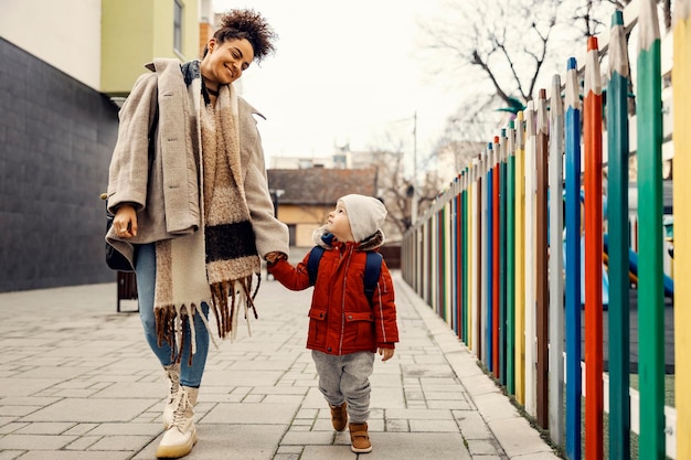 Een gelukkige jonge vrouw hand in hand met kleine jongen met een schooltas op zijn rug