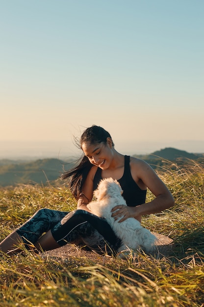 Een gelukkige jonge vrouw zittend op het gras te spelen met haar mooie puppy hondje