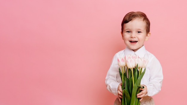 Een gelukkige jongensheer heeft een boeket delicate roze tulpen in zijn handen. Ruimte voor uw tekst, kopieer ruimte