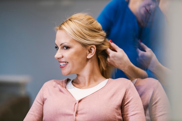 Foto een gelukkige klant kijkt zichzelf in een spiegel in een salon terwijl de kapper vlecht maakt