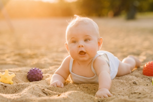 Een gelukkige kleine jongen ligt op een zandstrand bij de zee in de stralen van de ondergaande zon