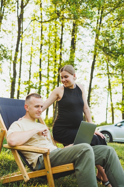 Een gelukkige man en zijn zwangere vrouw werken op een laptop terwijl ze in de natuur zitten Een jong stel ontspant in de natuur en kijkt een film op een laptop