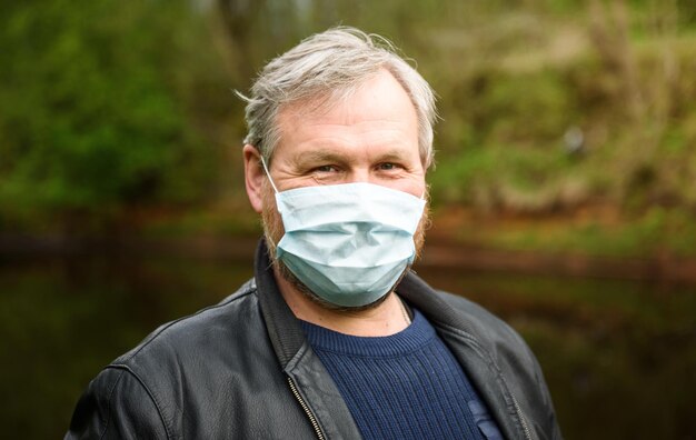 Een gelukkige man op een natuurwandeling langs de rivier met een medisch masker verheugt zich aan het einde van de quarantaine