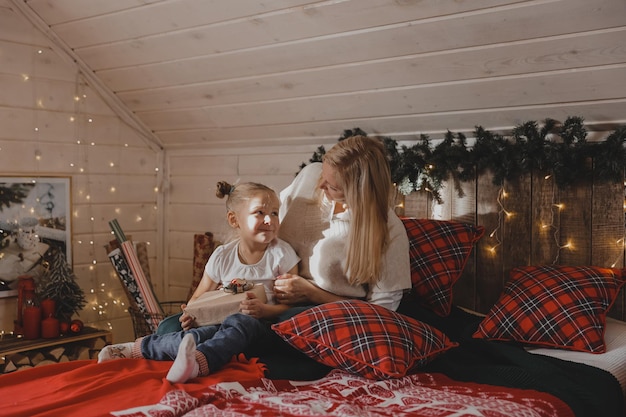 Een gelukkige moeder en dochter met kerstcadeaus zitten op een bed in een met kerst versierde slaapkamer