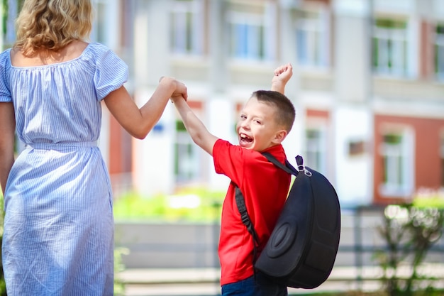 Een gelukkige moeder leidt het kind naar school op de terugweg naar school