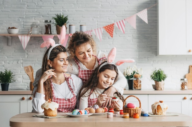 Een gelukkige moeder met haar volwassen dochters schildert paaseieren thuis in de keuken