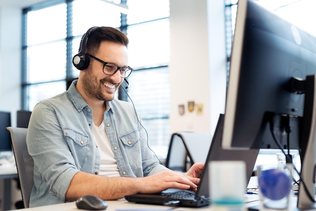 Een gelukkige programmeur werkt op zijn computer met een koptelefoon op.