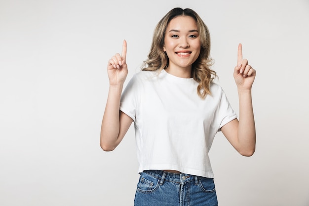 een gelukkige schattige jonge vrouw poseren geïsoleerd over een witte muur muur wijzend