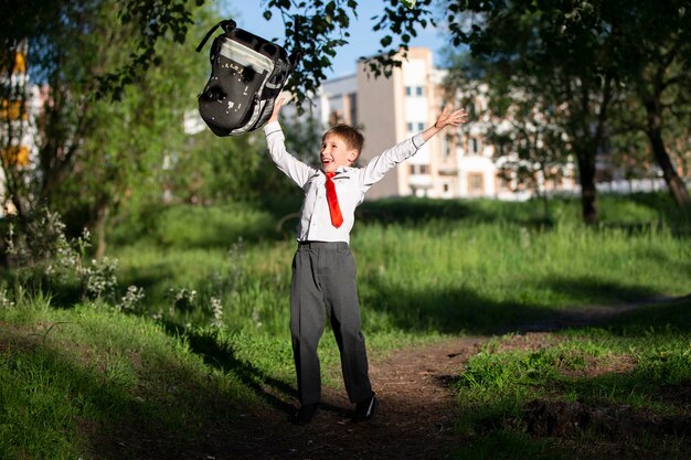 Een gelukkige schooljongen gooit zijn schoolrugzak over en verheugt zich aan het begin van de vakantie