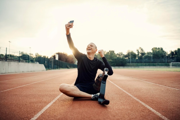 Een gelukkige sportman met kunstbeen die in het stadion zit en selfies maakt