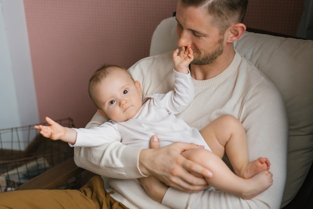 Foto een gelukkige, tevreden vader houdt zijn zoontje in zijn armen en zit thuis in een leunstoel