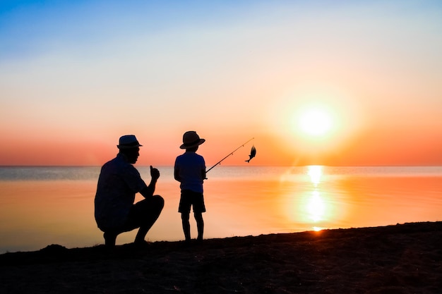 Een gelukkige vader en kindvissers vangen vis bij de zee op natuursilhouet reizen