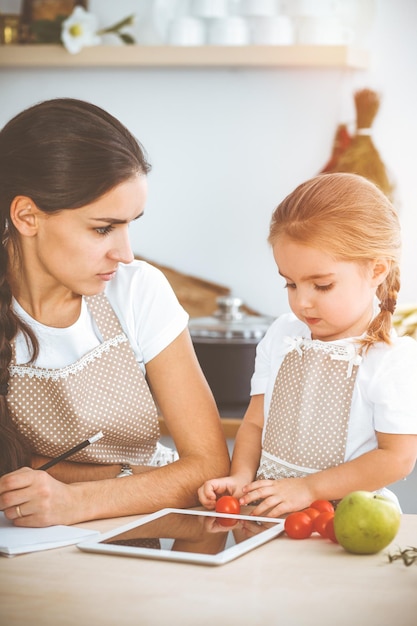 Een gelukkige vrouw en haar dochter zijn op zoek naar nieuwe recepten voor een familiefeest in de zonnige keuken