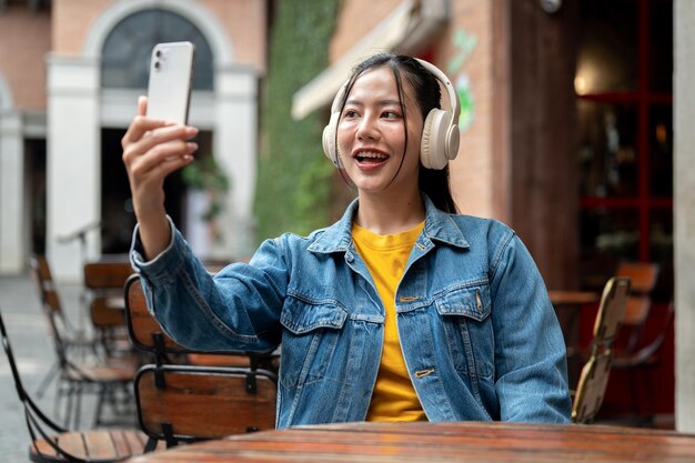 Een gelukkige vrouw gebruikt haar telefoon om een selfie te maken terwijl ze aan een buitentafel van een restaurant zit