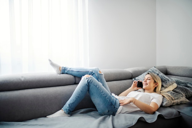 Een gelukkige vrouw geniet van het telefoongesprek terwijl ze op de bank ligt