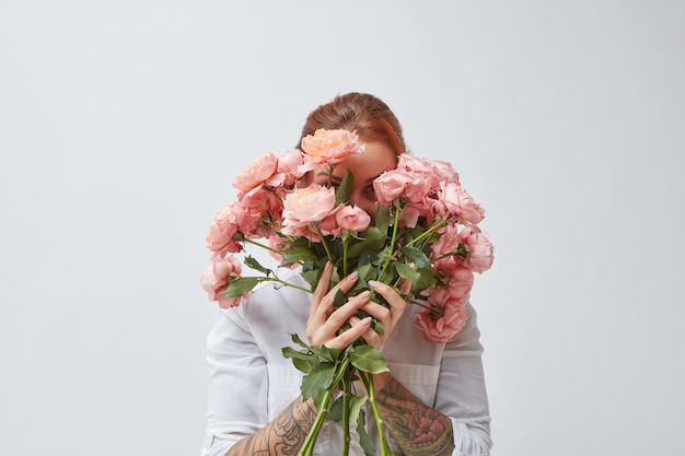 Een gelukkige vrouw met een tatoeage op haar handen verbergt haar gezicht achter een boeket geurige roze rozen. Moederdag