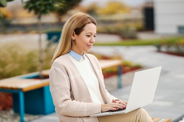 Een gelukkige vrouw zit in een park in het centrum en typt een verslag op een laptop