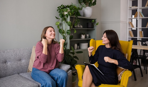 Een gelukkige vrouwelijke cliënt zit op de bank en communiceert met een psycholoog-vrouw in de kamer. Blij met succes