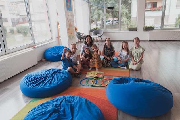 Een gelukkige vrouwelijke lerares zit en speelt handspelletjes met een groep kleine schoolkinderen