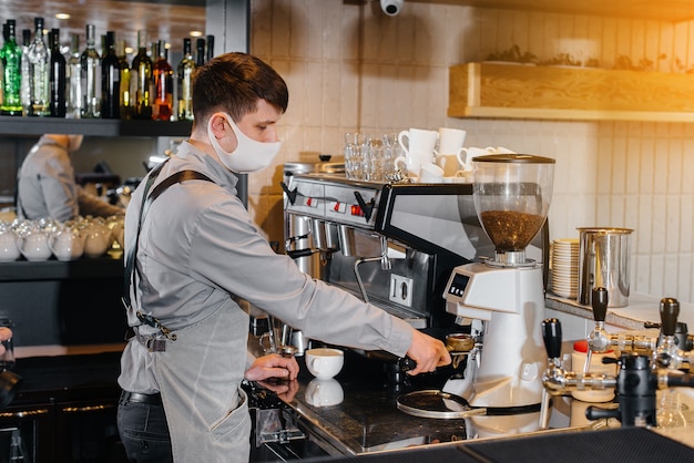 Een gemaskerde barista bereidt heerlijke koffie aan de bar in een café. Het werk van restaurants en cafés tijdens de pandemie.