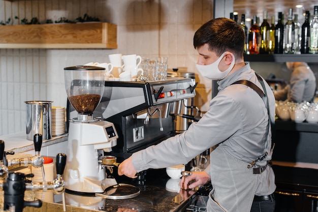 Een gemaskerde barista bereidt heerlijke koffie aan de bar in een café. Het werk van restaurants en cafés tijdens de pandemie.