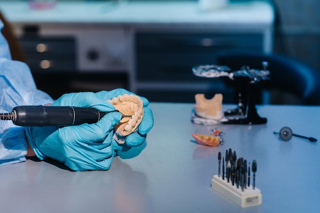 Een gemaskerde en gehandschoende tandtechnicus werkt aan een prothetische tand in zijn laboratorium