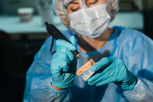 Een gemaskerde en gehandschoende tandtechnicus werkt aan een prothetische tand in zijn laboratorium.
