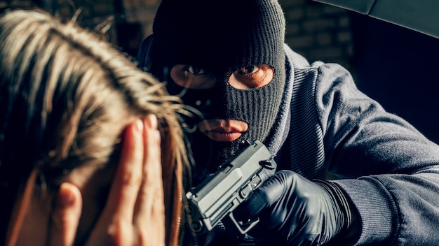 Foto een gemaskerde overvaller met een pistool bedreigt een vrouw in een auto. beroving