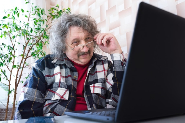 Een gepensioneerde met een bril die thuis achter de computer werkt, ouder wordende levensstijl