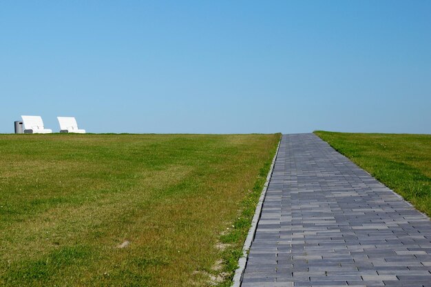 Een geplaveid pad leidt door een weide naar de hemel en aan het einde is er een bankje