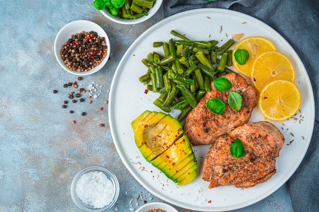 Een gerecht met kip en groenten, citroen en avocado op een grijze betonnen achtergrond.