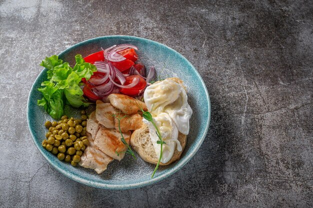 Een gerecht serveren van de menukaart van het restaurant. Kipfilet met groenten en Groenen, tomaten, uien, omeletten en groene erwten op een bord tegen de achtergrond van een grijze stenen tafel