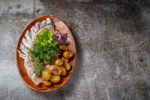 Een gerecht serveren van een restaurantmenu. Gezouten gesneden haringvis met ingemaakte champignons en uien, roomsaus, dille en peterseliegroen op een bord tegen de achtergrond van een grijze stenen tafel