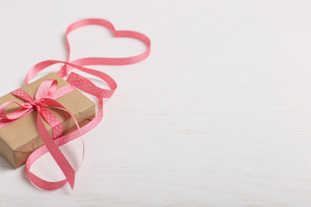 Een geschenk van ambachtelijk papier en een roze lint op een witte houten tafel