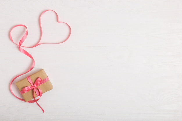 Een geschenk van ambachtelijk papier en een roze lint op een witte houten tafel