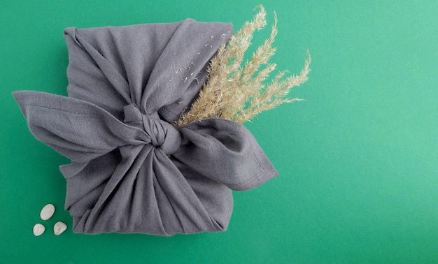 Een geschenk verpakt in een grijs linnen servet met takken van pampagras op een groene achtergrond met ruimte voor tekst Milieuconcept
