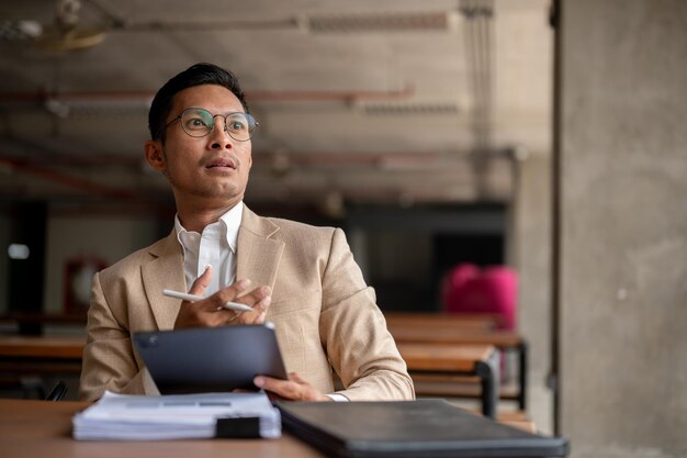 Foto een geschokte verbaasde aziatische millennial zakenman met een digitale tablet en een pen die aan tafel zit