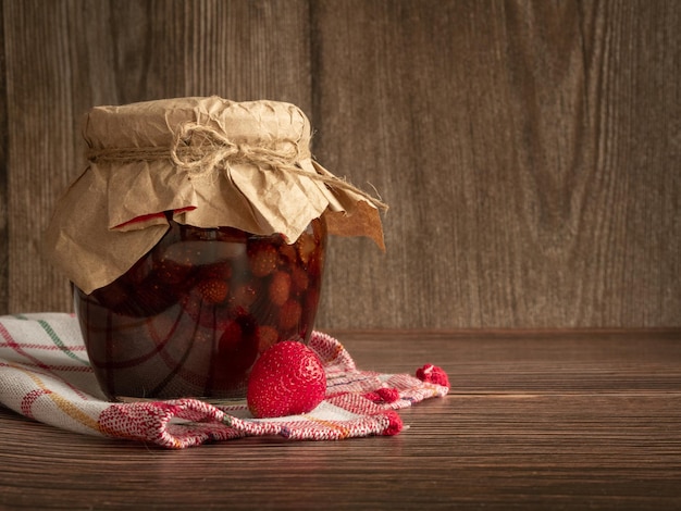 Foto een gesloten pot aardbeienjam op een houten ondergrond met perkament en jute touw