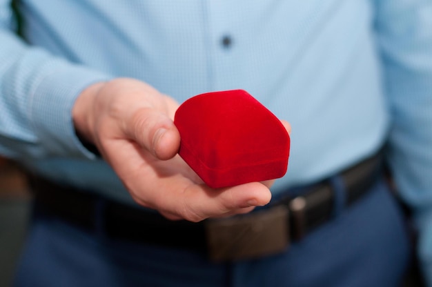 Een gesloten roodfluwelen ringdoosje in de handen van een man in een blauw shirt