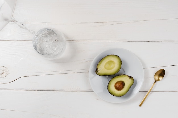 Een gesneden avocado op een witte plaat naast een glas water op een tafel