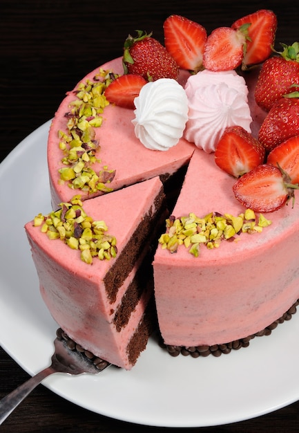 Een gesneden stuk chocolade-aardbeienmousse cake versierd met bessen, meringue en pistachenoten